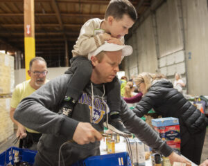 Kid on the shoulders of an adult while sorting food at the JFS Community-Wide Food Sort.